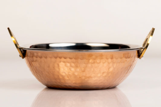 Hammered copper serving bowl with brass handles and dark interior lining.