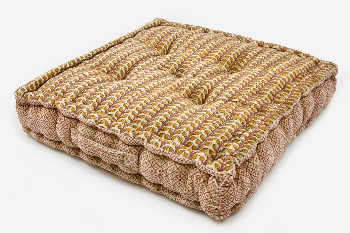 Square cushion with geometric block print pattern in gold, cream, and rust tones with quilted top and textured sides.