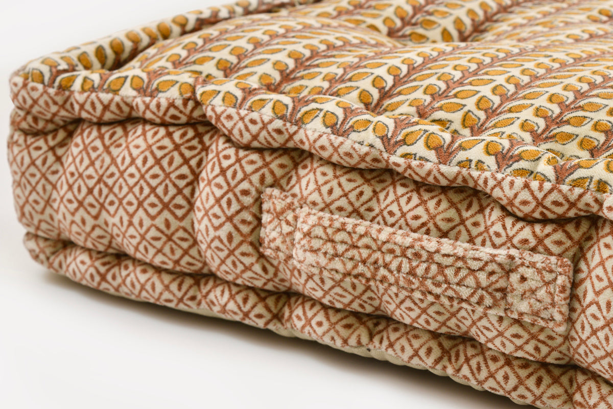 Square meditation cushion with tan and cream block print geometric pattern and quilted surface.