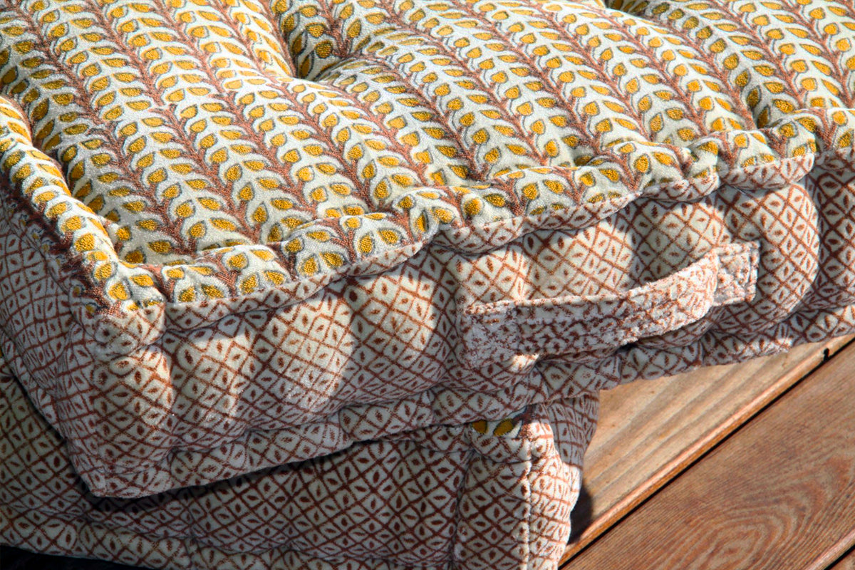 Square meditation cushion with yellow and white block print pattern on top and geometric patterned fabric on sides.