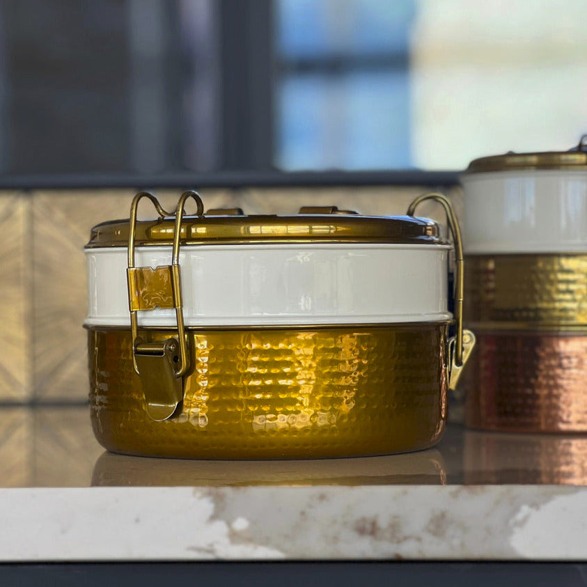 Gold hammered stainless steel tiffin lunch box with white band and brass latch handles.