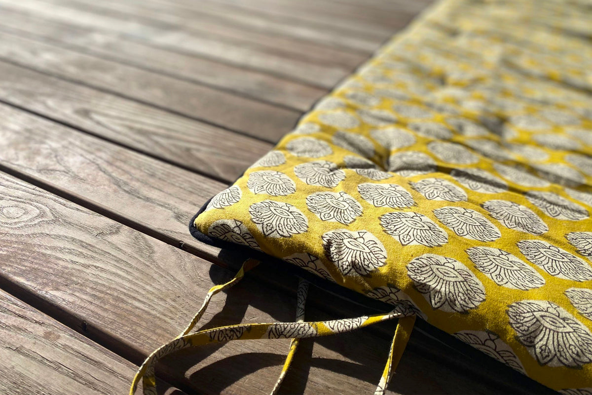 Yellow and white block print yoga mat with shell pattern and matching carrying handles on wooden surface.