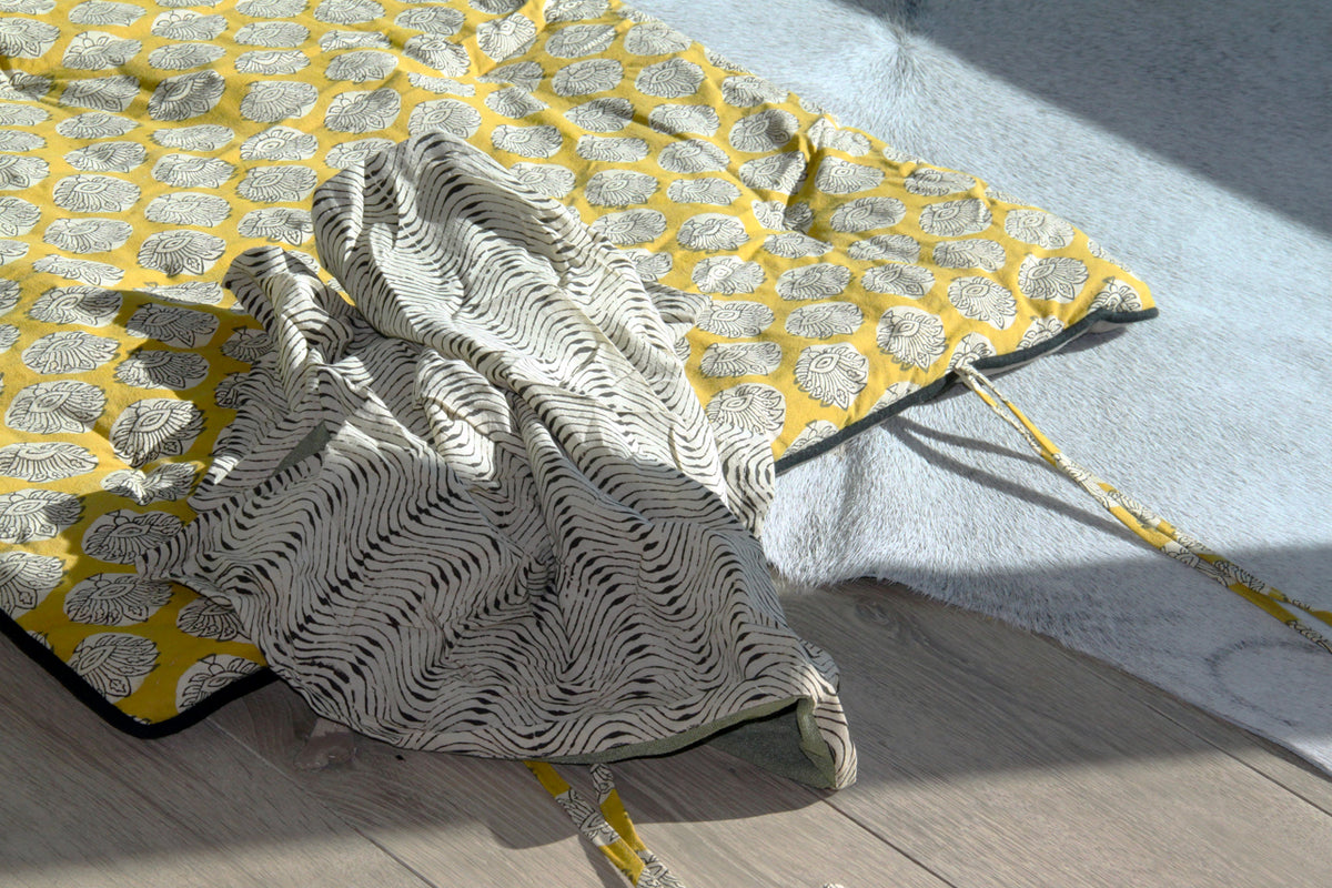 Yellow block print yoga mat with white floral pattern, rolled with matching towel and black carrying strap.
