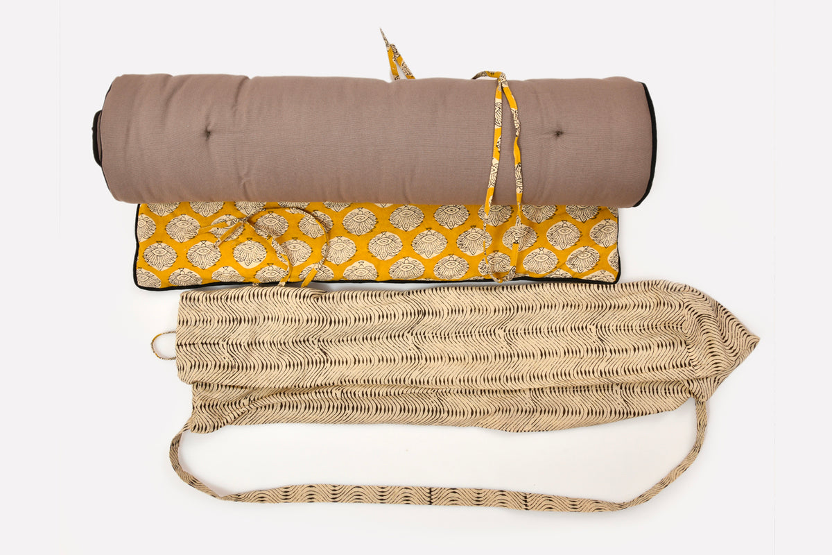 Rolled taupe yoga mat with yellow block print carrying case and woven towel displayed flat.