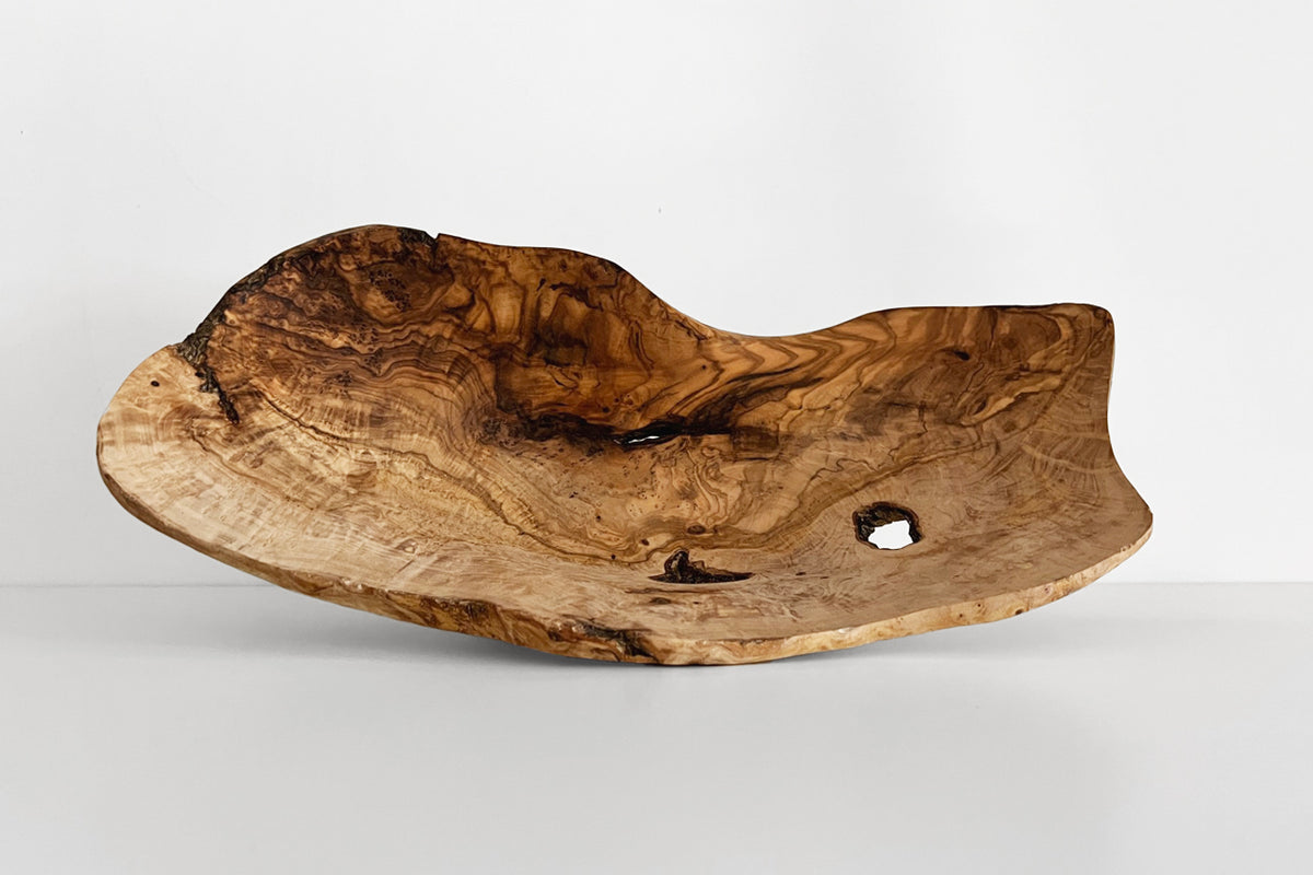 Organic olivewood bowl with natural grain patterns, irregular edges, and carved interior depression.