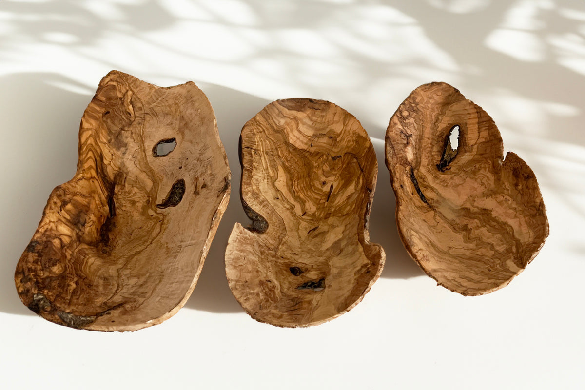 Three organic olivewood bowls with natural grain patterns and irregular edges carved from root sections.
