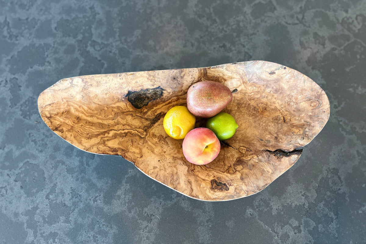 Irregular wooden bowl with natural grain patterns holding lemons, limes, and apples.