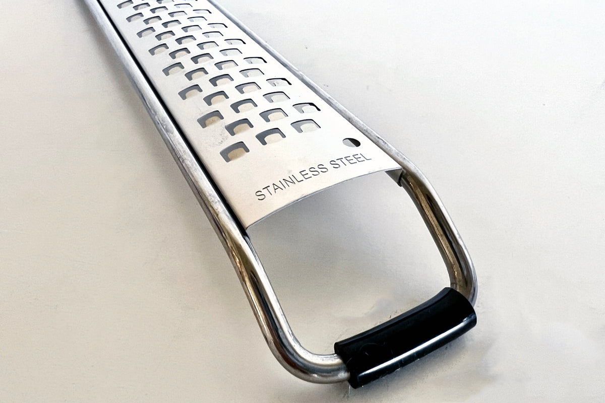Stainless steel paddle grater with perforated grating surface and black handle grip.