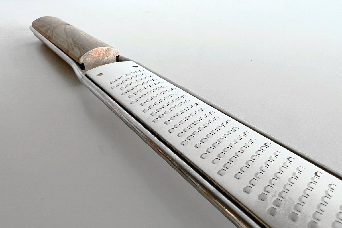 Wooden-handled paddle grater with metal grating surface and small holes arranged in rows.