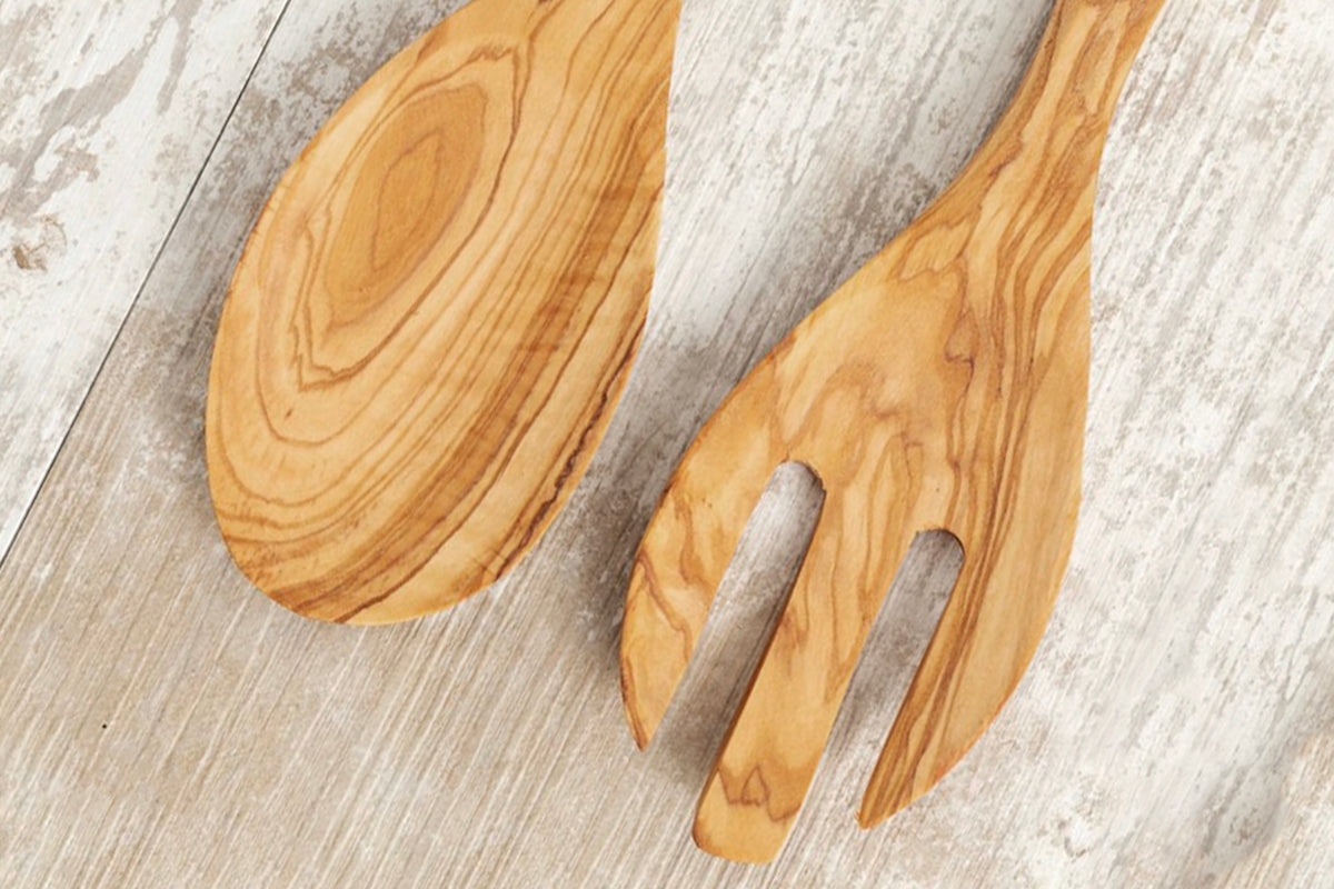 Pair of wooden salad servers with oval and fork-shaped bowls on whitewashed wood surface.