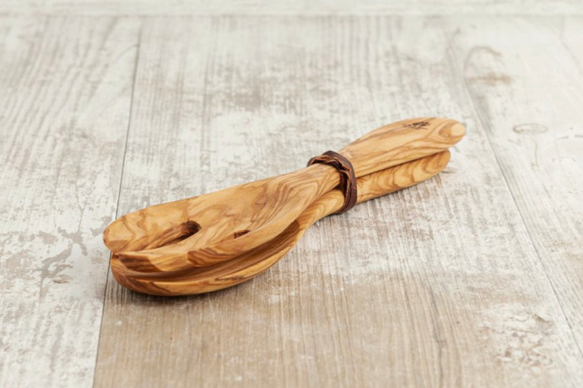 Pair of wooden salad servers with natural grain pattern and leather cord tie on whitewashed wood surface.