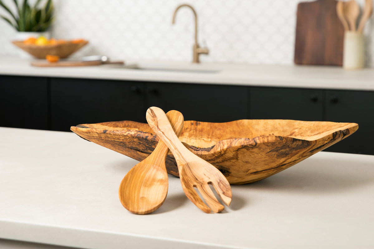 Pair of wooden salad servers with slotted bowls and a matching wooden serving bowl on white countertop.
