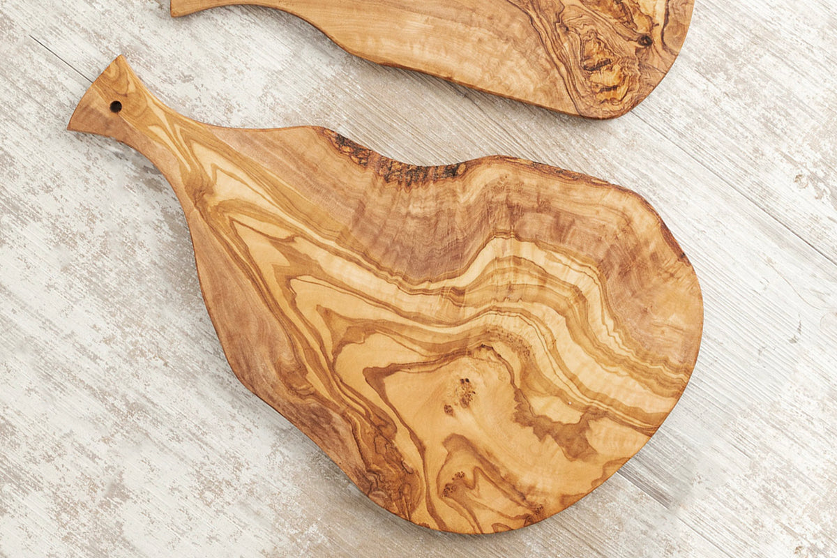 Olive wood charcuterie board with paddle handle and natural grain patterns on whitewashed surface.