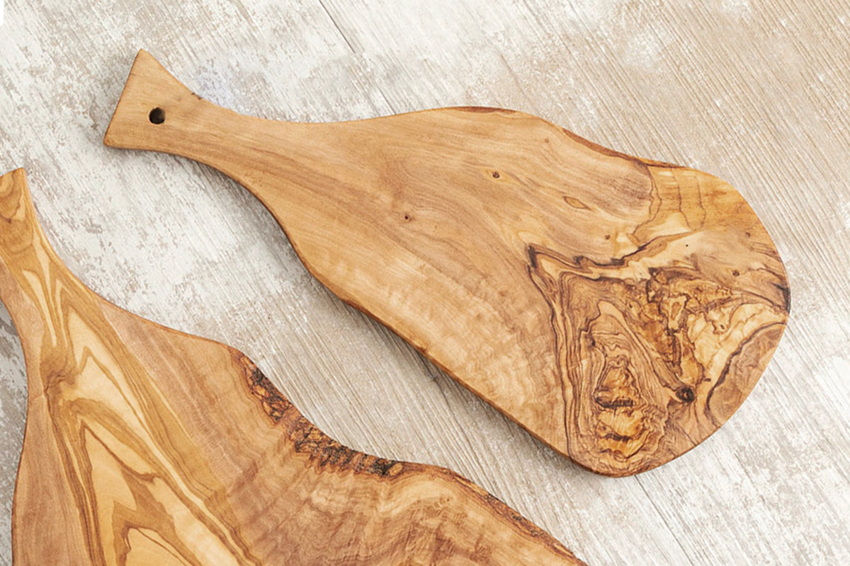 Olive wood charcuterie boards with paddle handles and natural grain patterns on whitewashed surface.