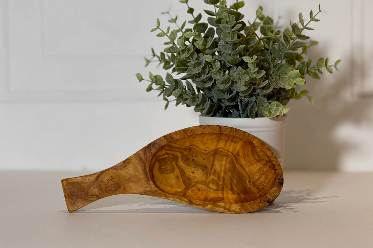 Olive wood bowl with handle in teardrop shape, showing natural grain patterns and carved detail.