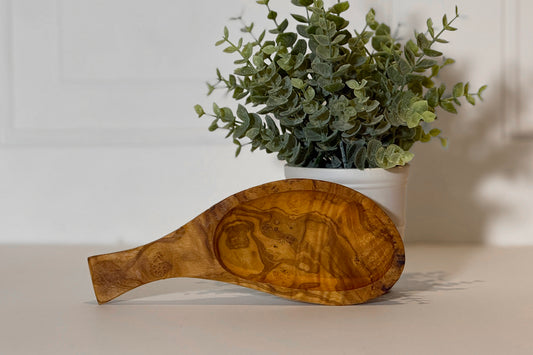 Olive wood bowl with handle in teardrop shape, showing natural grain patterns and carved detail.