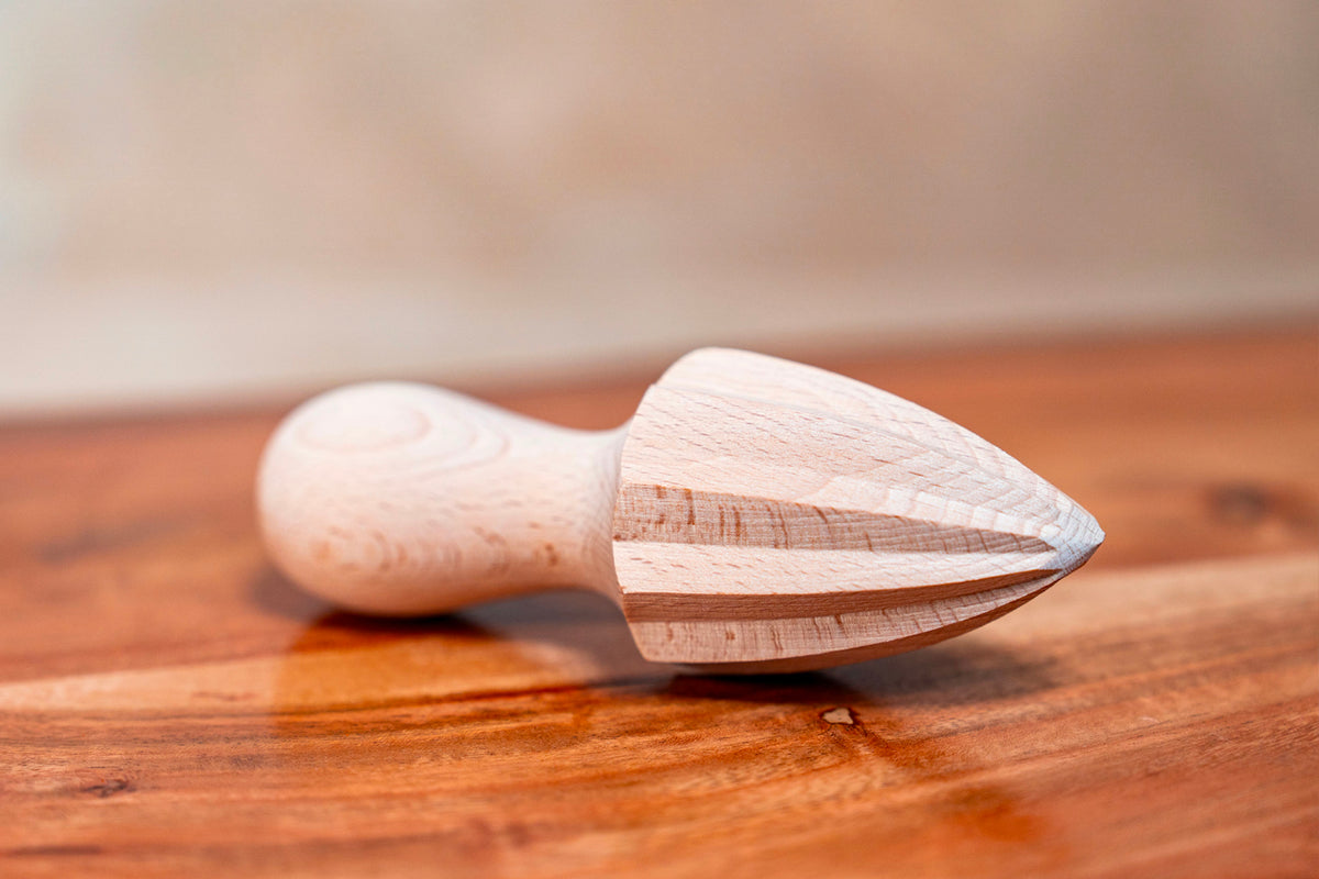 Wooden citrus reamer with tapered conical head and rounded handle, displayed on a wooden surface.