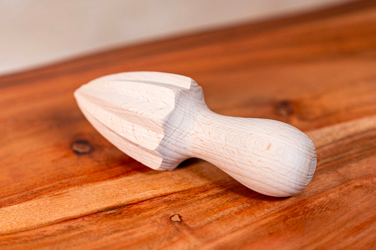Light wood citrus squeezer with curved handle and ribbed reaming cone on wooden surface.