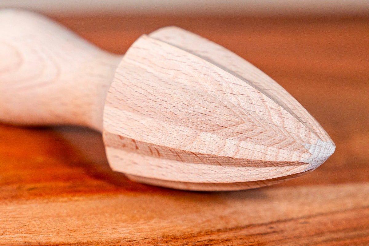 Wooden citrus reamer with light beechwood cone and handle, displayed on brown surface.