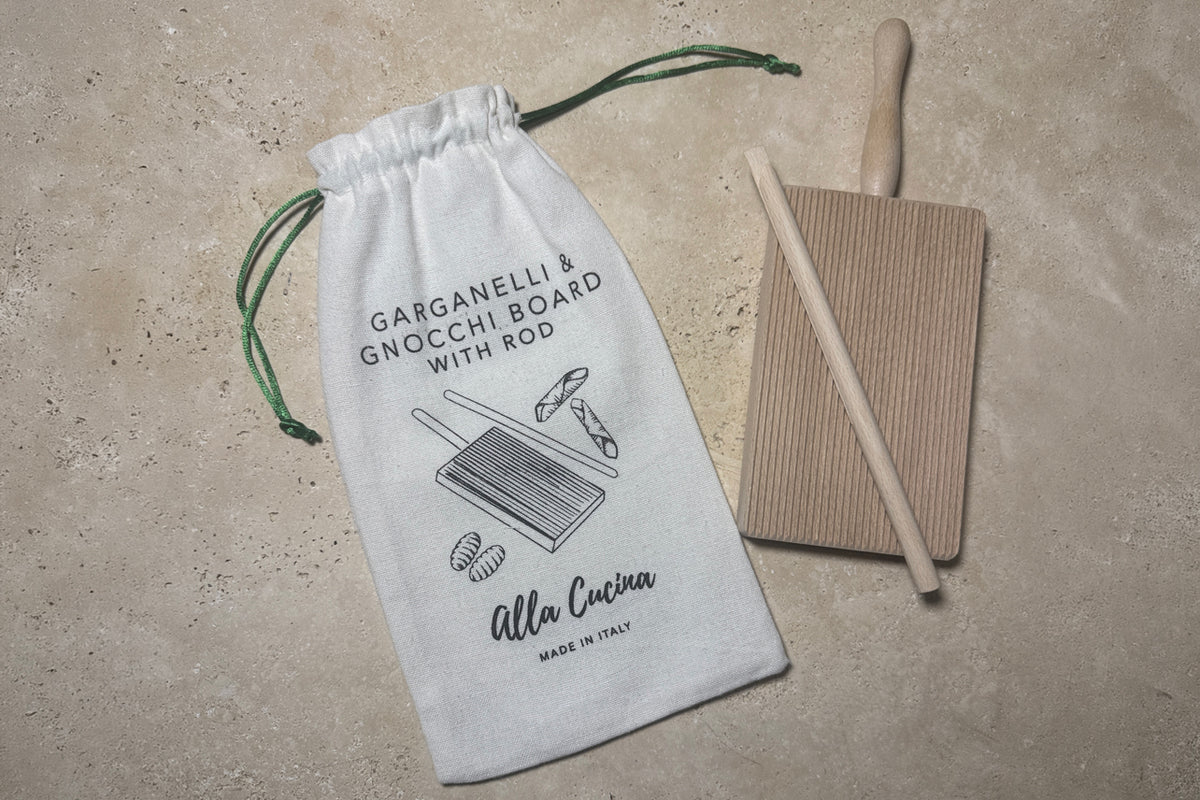 Wooden gnocchi and garganelli board with rolling pin and white cotton drawstring storage bag on concrete surface.