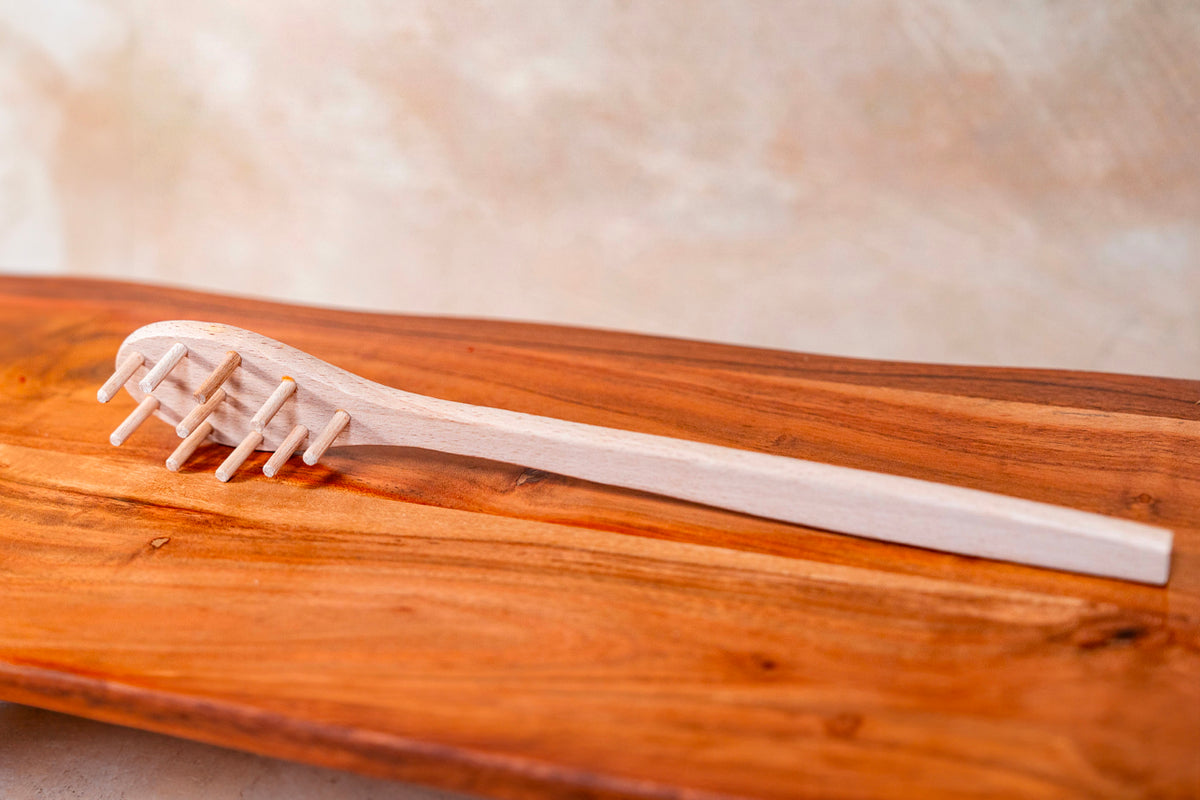 Pale wooden spaghetti fork with four tines resting on a darker wood surface.