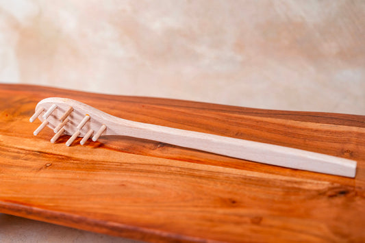 Pale wooden spaghetti fork with four tines resting on a darker wood surface.