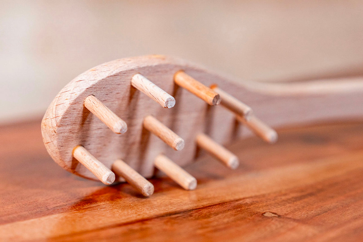 Wooden spaghetti fork with light-colored round head and multiple short prongs lying on a wooden surface.