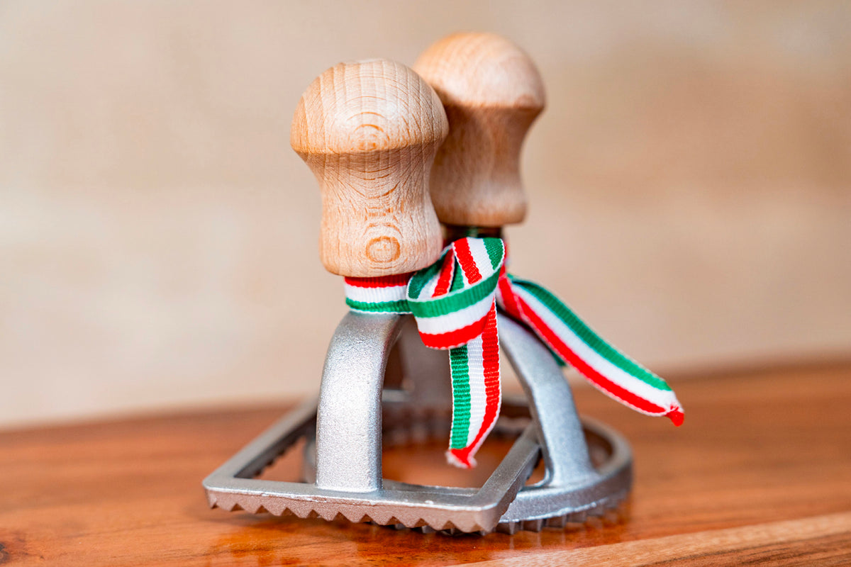 Wooden-handled ravioli stamp with metal base and Italian flag ribbon, featuring circular cutting surface with grid pattern.