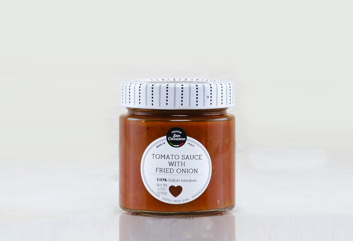 Glass jar of tomato sauce with fried onion and patterned white lid on gray background.