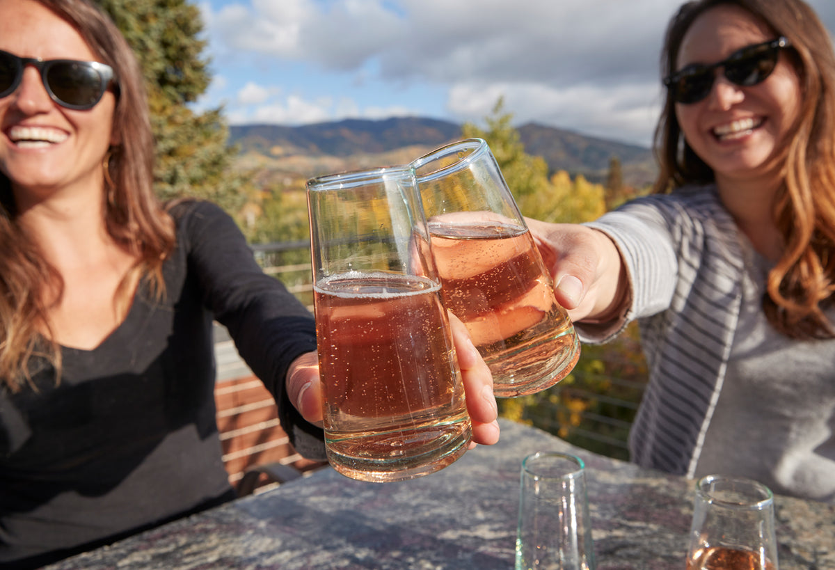 Set of six clear cone-shaped champagne glasses filled with sparkling beverage, held by two people outdoors.