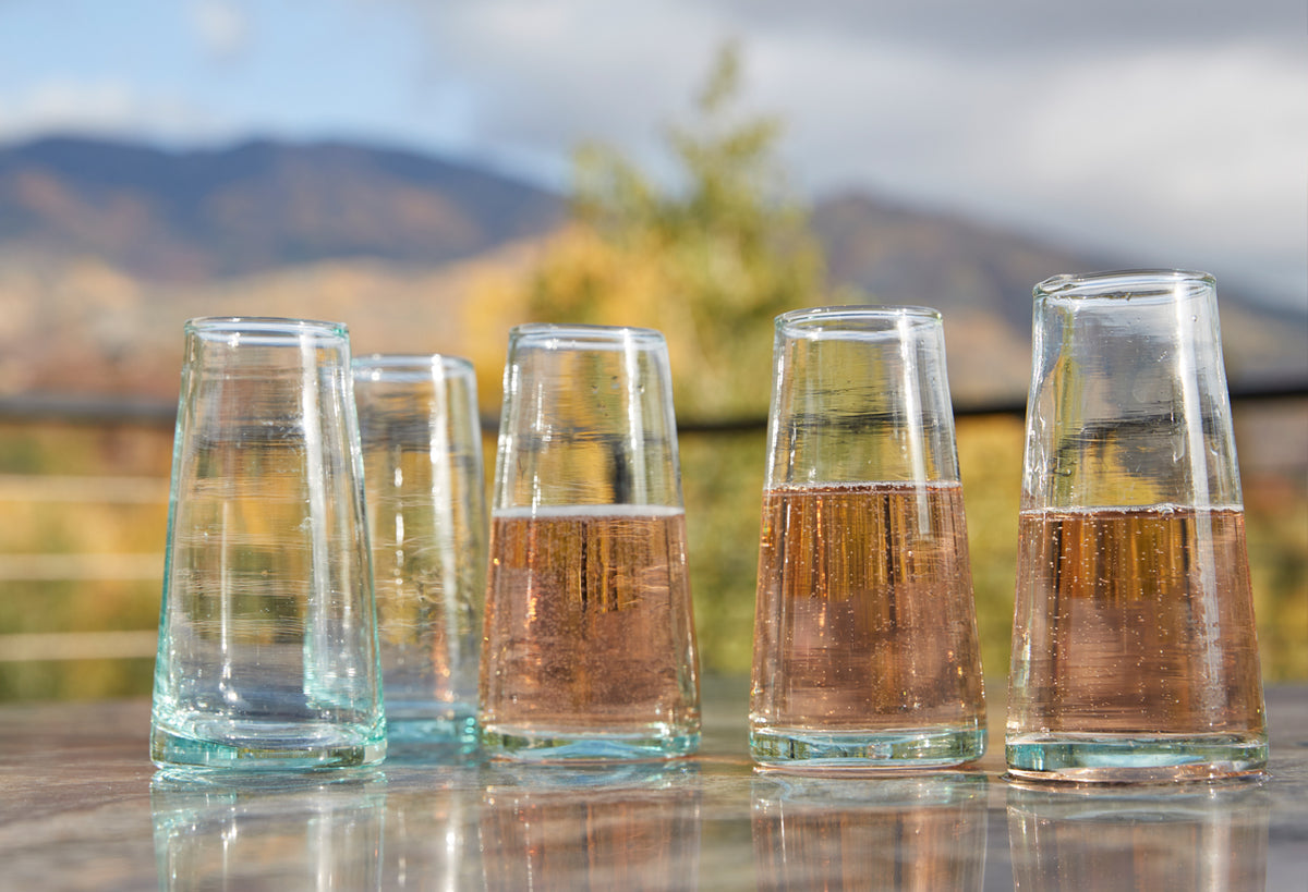 Six cone-shaped champagne glasses with clear glass bases, some containing champagne and others empty.