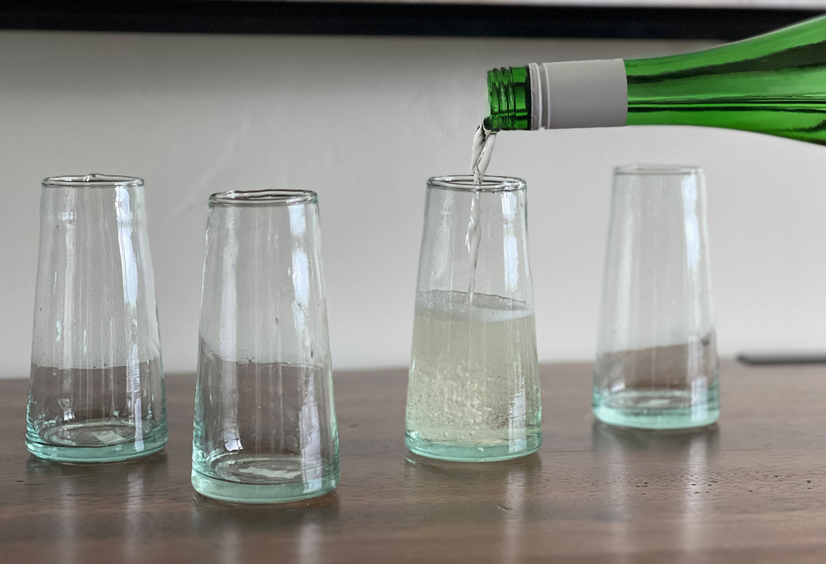 Four cone-shaped champagne glasses with green tinted bases, one being filled from a green bottle.
