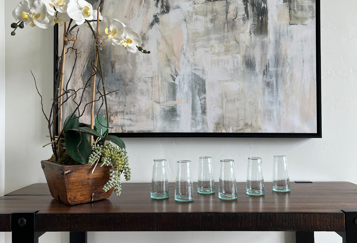 Set of six clear cone-shaped champagne glasses with turquoise bases lined up on a wooden table.
