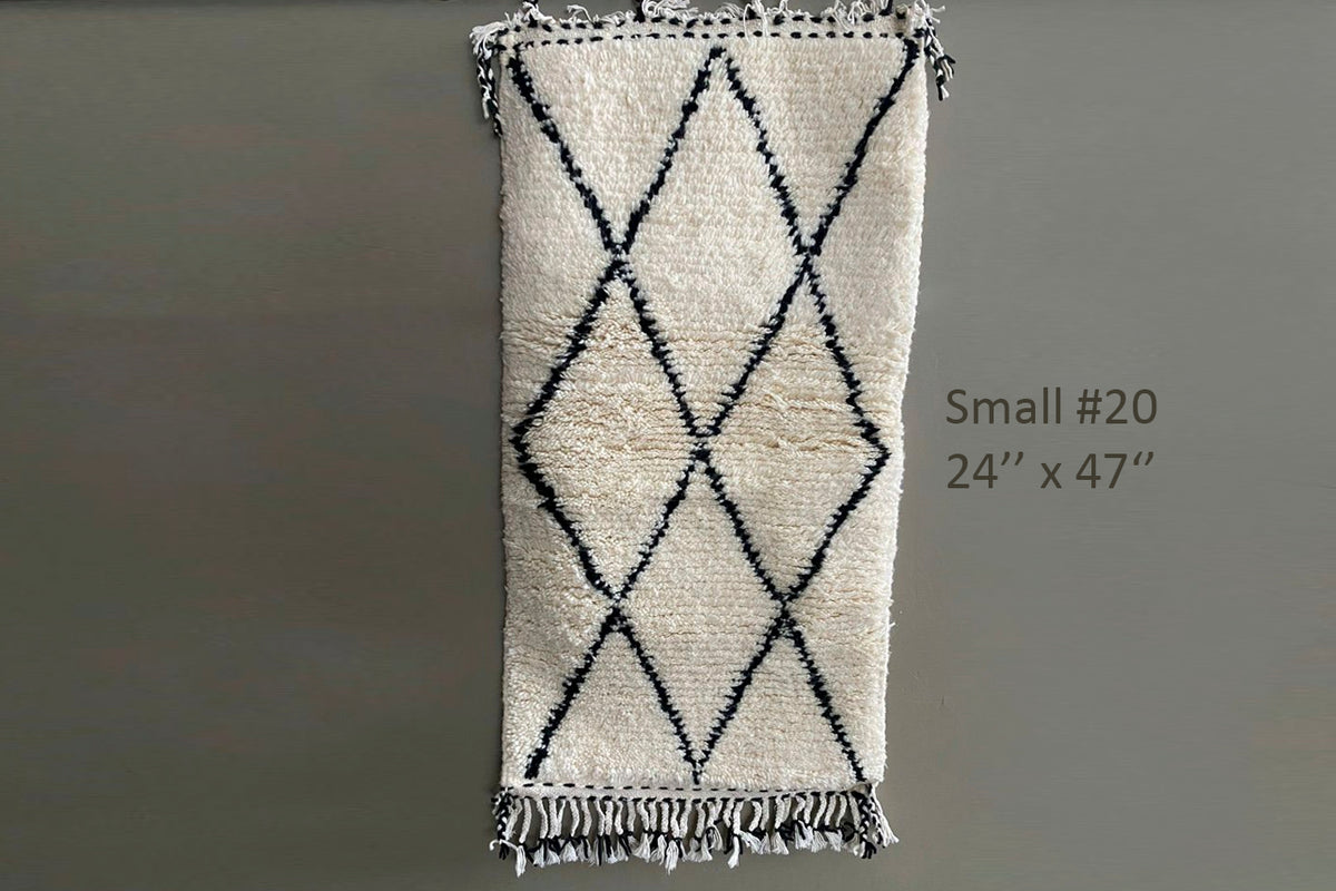 Cream-colored handwoven rug with black diamond pattern and tasseled ends, 24" x 47".
