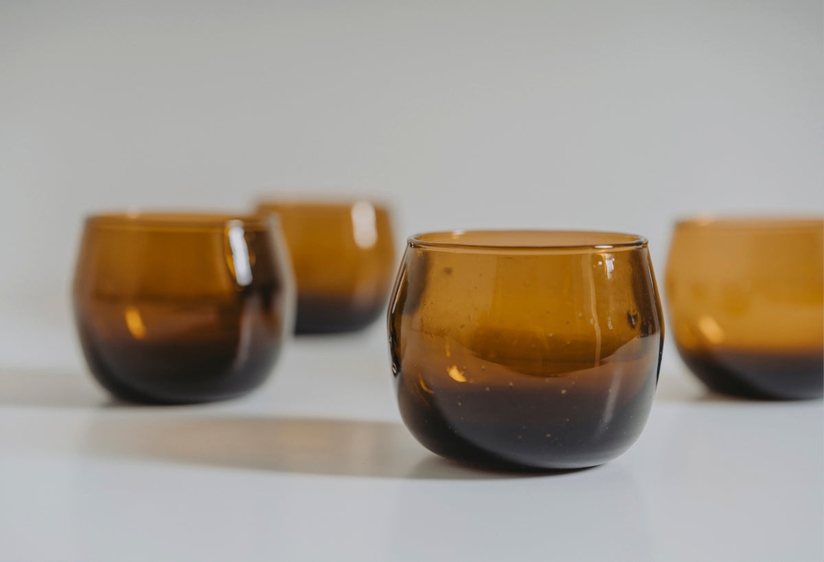 Four amber glass stemless goblets with rounded bowls and gradient coloring from dark brown to golden amber.