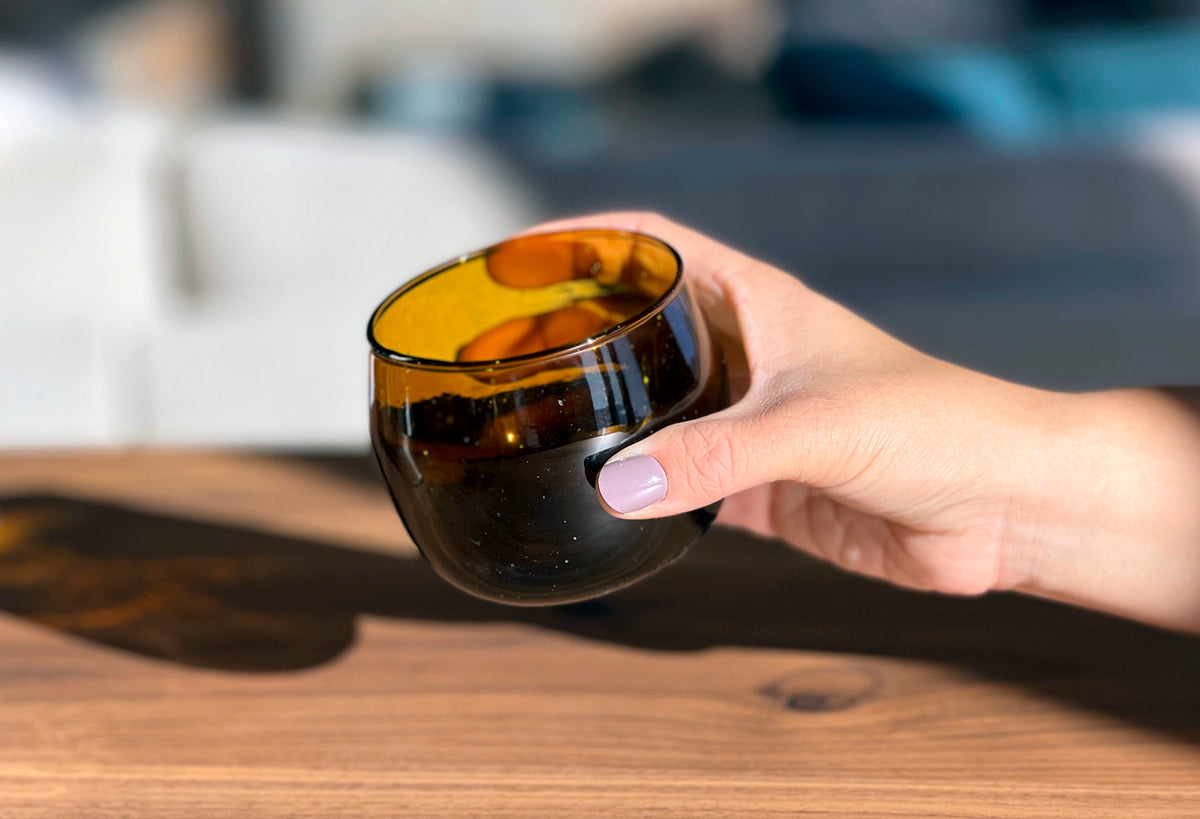 Hand holding amber-tinted stemless glass goblet with dark band accent.