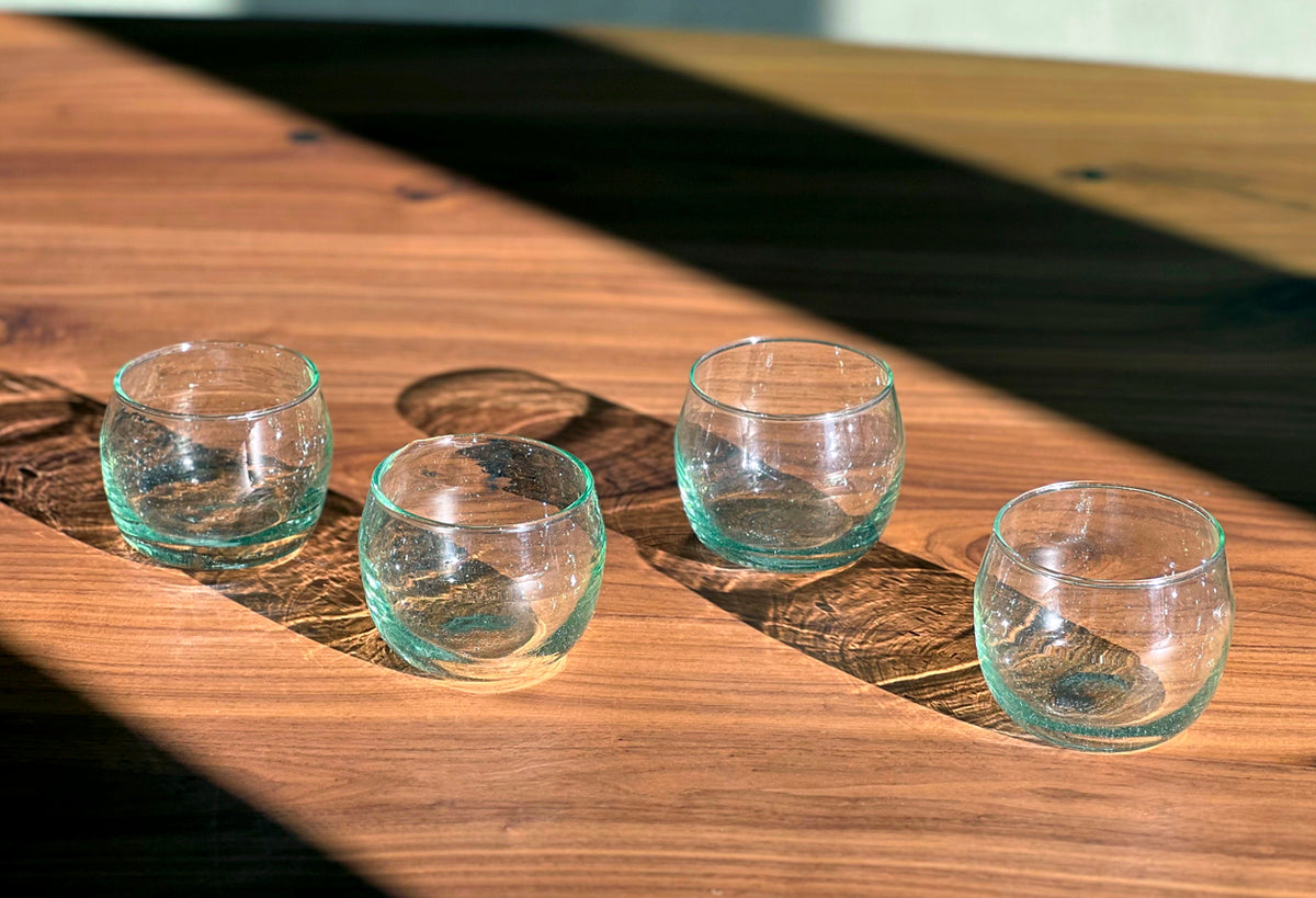 Four clear glass stemless goblets with green-tinted bases arranged on a wooden surface.