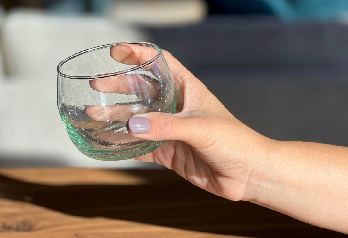 Clear glass stemless goblet with green tinted base held in hand.