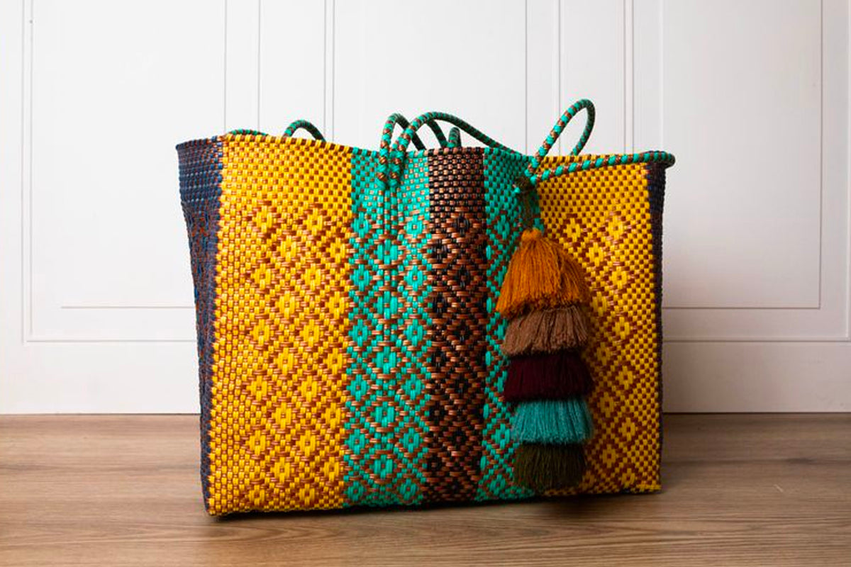 Woven tote bag with yellow, teal, and brown geometric pattern and multi-colored tassel charm.