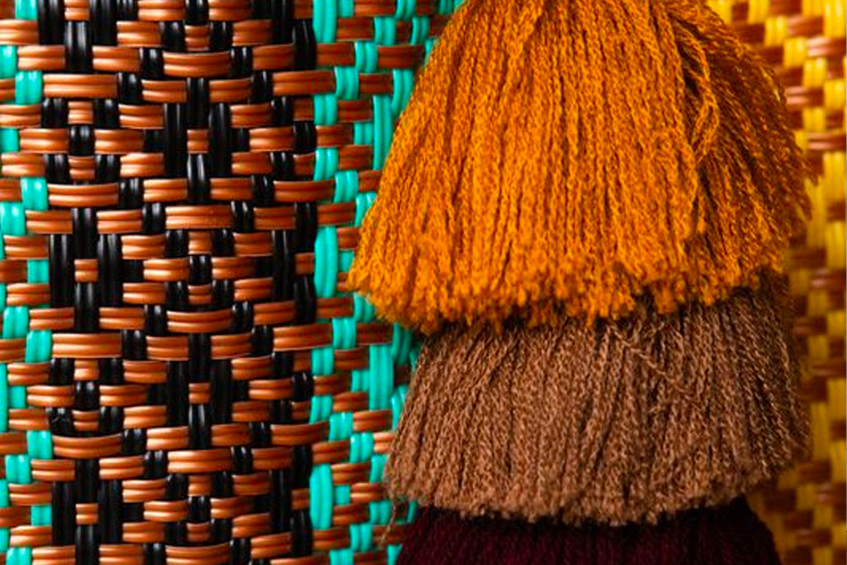 Woven tote bag with orange, brown, and black geometric pattern, featuring fringe trim in orange and brown tones.