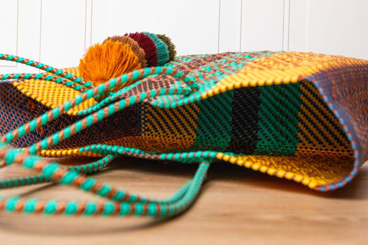 Woven tote bag with multicolor geometric pattern in yellow, green, teal, and burgundy, featuring matching braided handles and