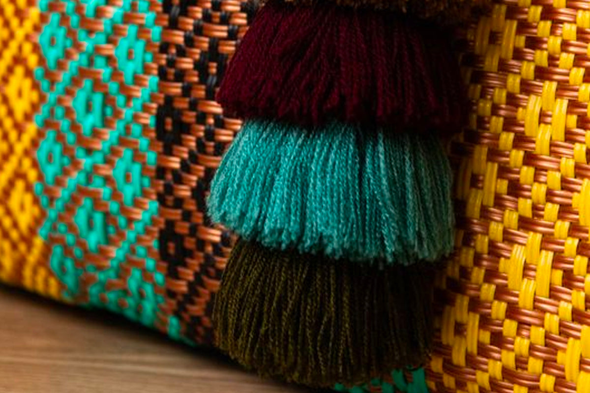 Woven tote bag with turquoise, orange, and yellow geometric patterns and burgundy, teal, and olive fringe trim.