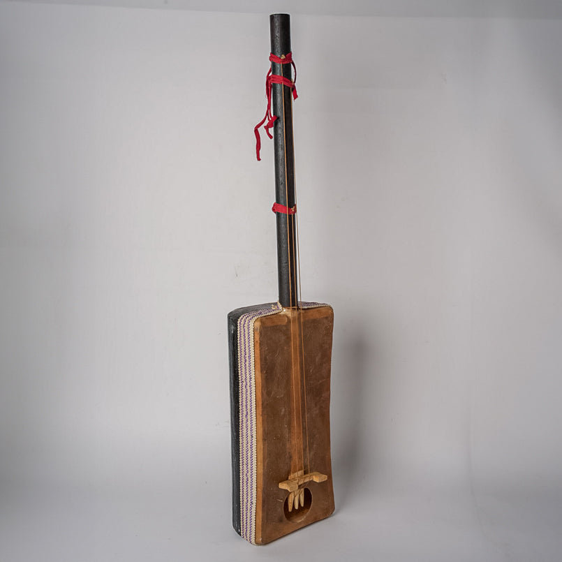 Wooden gimbri with black neck, red fabric binding, and carved decorative detail on the body.