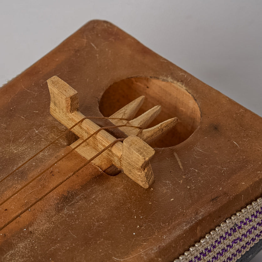 Wooden gimbri with sound hole and three tuning pegs, showing carved neck detail and woven fabric strap.