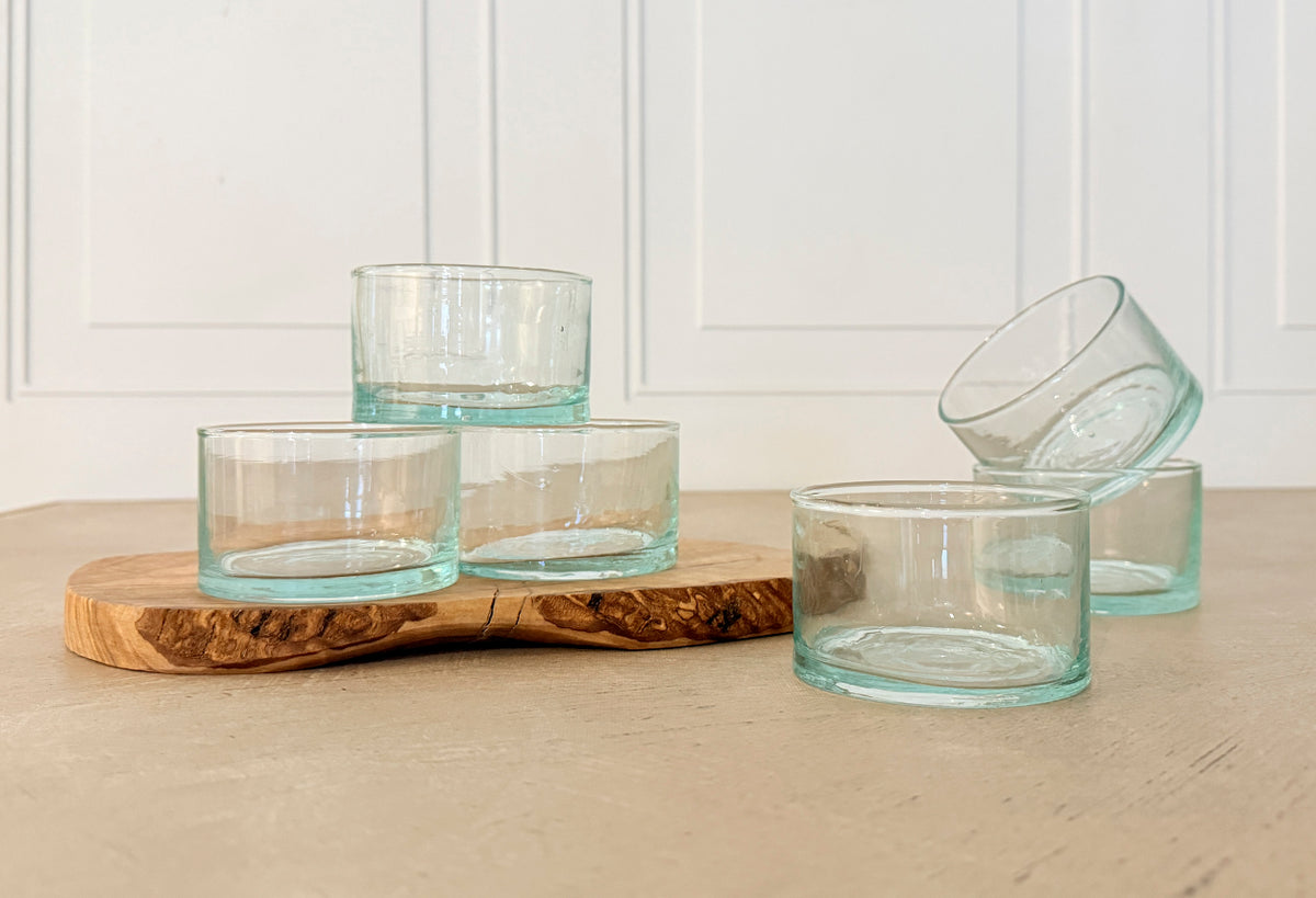 Six clear glass cups with turquoise-tinted bases arranged on a wooden surface.