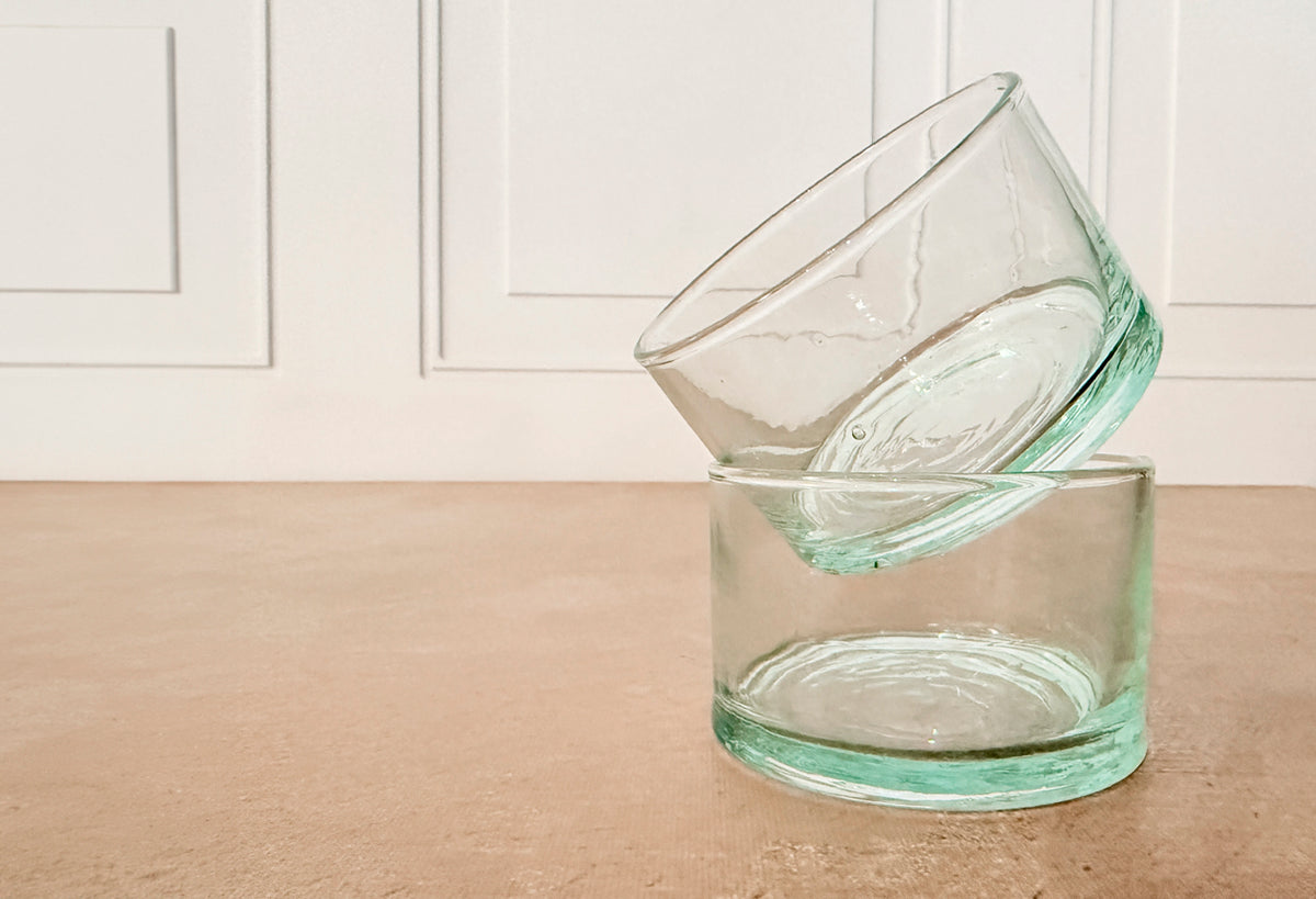 Two clear glass cups with green-tinted bases stacked together on a tan surface.