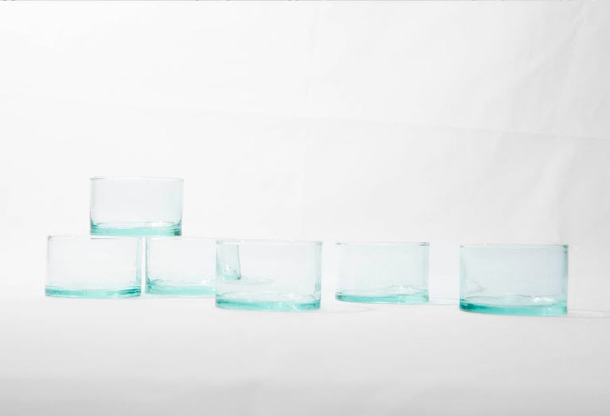 Six clear glasses with turquoise-colored bases arranged in a row on white background.