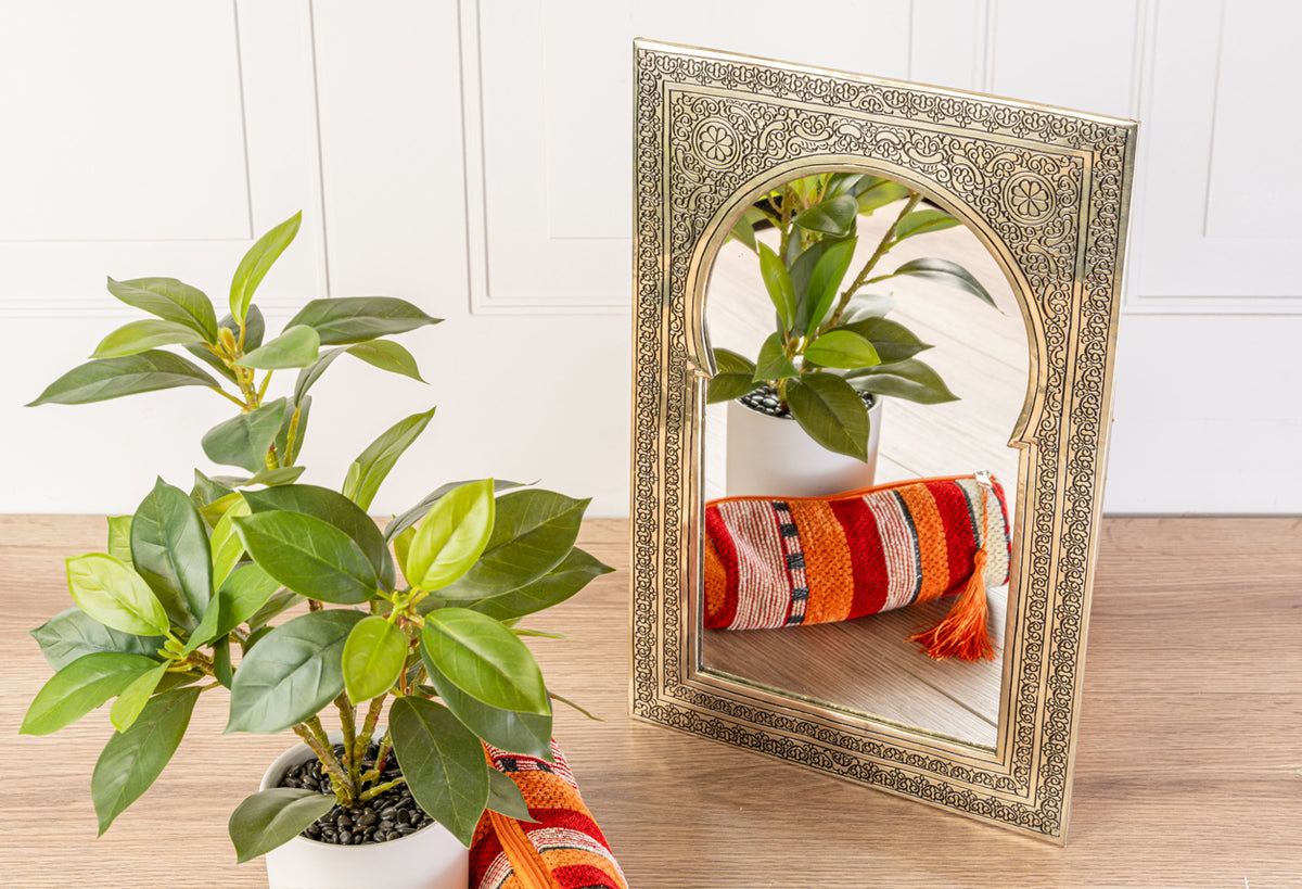 Ornate gold-framed mirror with intricate geometric patterns reflecting a potted plant and striped fabric.