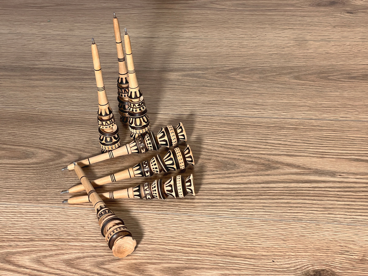 Six wooden molinillo pens with carved handles and metal decorative bands arranged on a wood surface.
