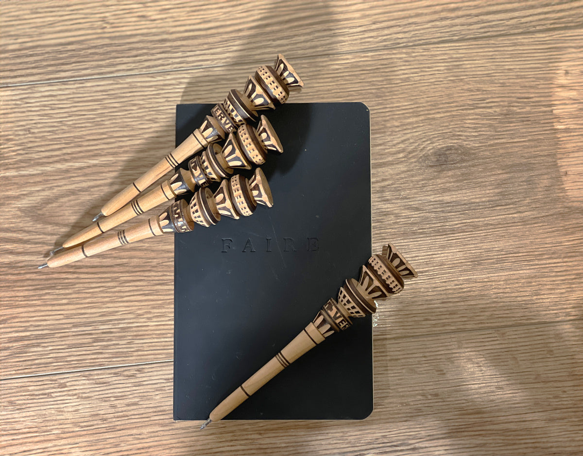 Wooden pens with decorative brass-colored bands at the top, arranged on a dark notebook.